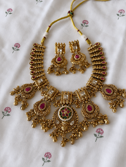 Gold necklace and earrings set on a floral-patterned fabric background