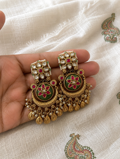 Decorative earrings held in a hand on a textured fabric background