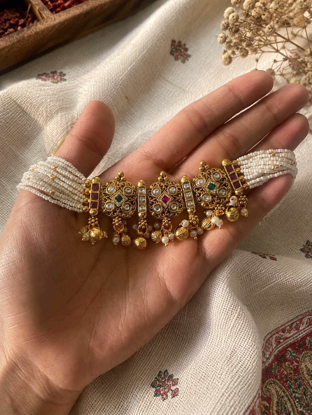 Decorative bracelet with gold and pearl details held in a hand on a patterned fabric background