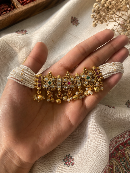 Decorative bracelet with gold and pearl details held in a hand on a patterned fabric background