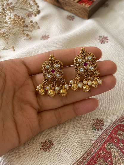 Gold earrings with pearls and red stones held in a hand on a patterned fabric background