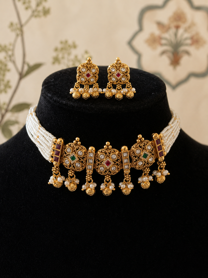Gold necklace and earrings set on a black stand with a floral background