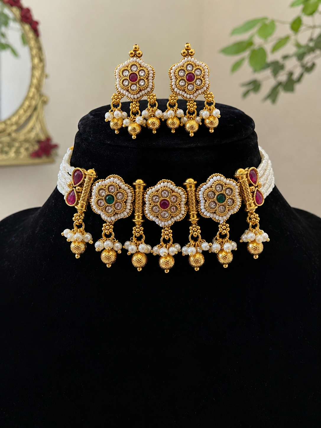 Gold jewelry set with necklaces and earrings on a black stand against a neutral background
