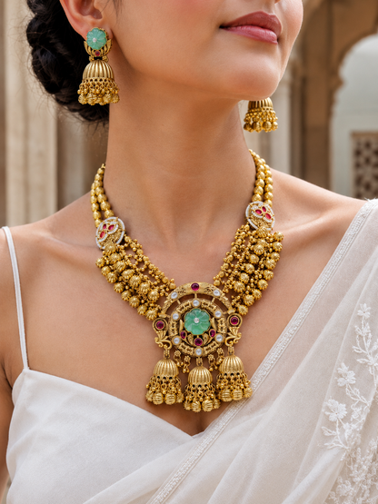 Close-up of a person wearing a gold necklace and earrings with gemstones.