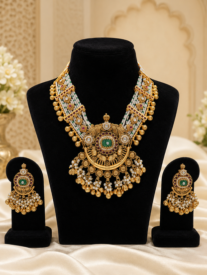 An elaborate antique gold-plated jewelry set displaying a multi-strand pearl necklace with a large circular statement pendant and matching drop earrings, adorned with green enamel centers, ruby red accents, and dense pearl fringe detailing on a black stand.