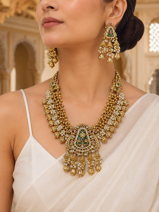 Woman wearing a gold necklace and earrings with a white saree in an indoor setting.
