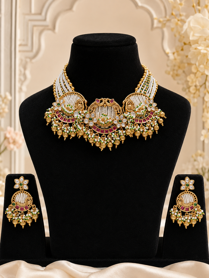 A royal traditional Indian bridal jewelry set displayed on black velvet busts. The set includes a heavy antique gold choke-style necklace and matching circular dangle earrings, adorned with intricate white seed pearl inlay panels, semi-circular crescent accents lined with deep red rubies, and tiered borders of hanging gold and tiny green accent beads.