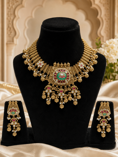 A luxurious antique gold Indian bridal necklace and earring set featuring a wide mesh-patterned collar, a large central pendant with a green stone, and intricate cascading gold bead clusters on a black mannequin display.
