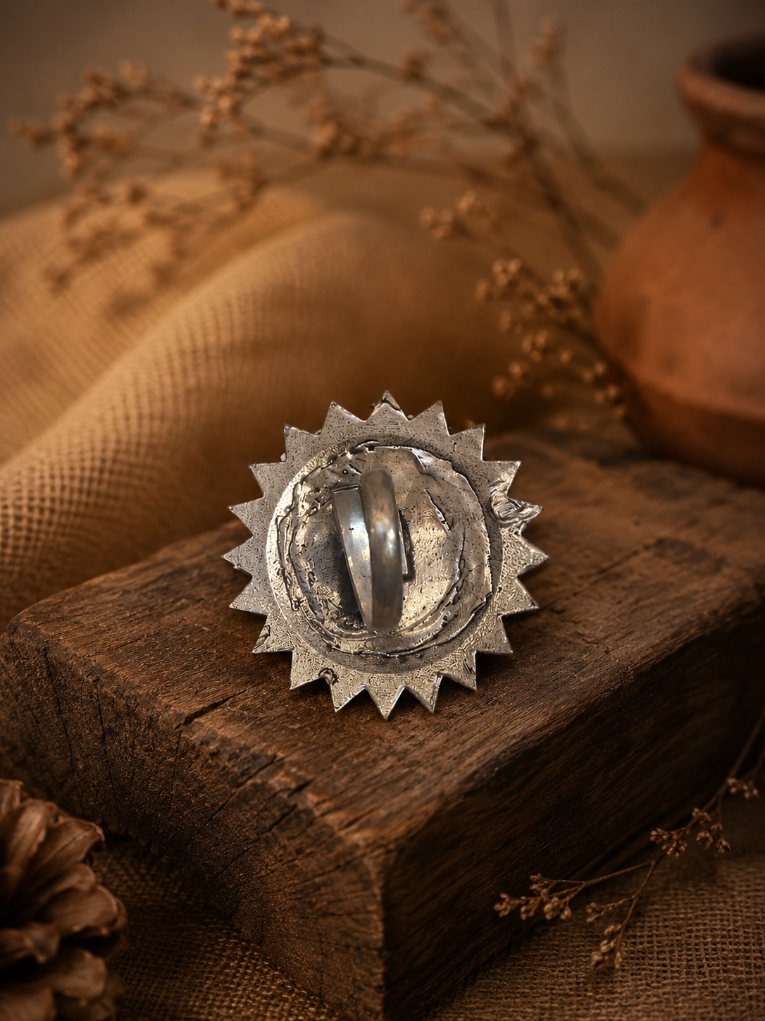 Silver sunburst design object on a wooden surface with a rustic background