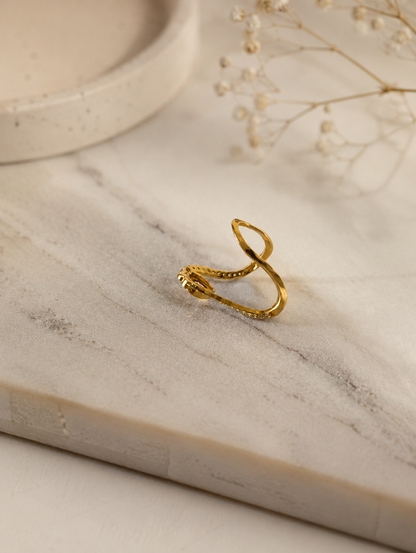 Side profile perspective of a gold-toned V-shaped Vanki ring laying on a white marble surface, showing the open curved band structure and stone setting details.