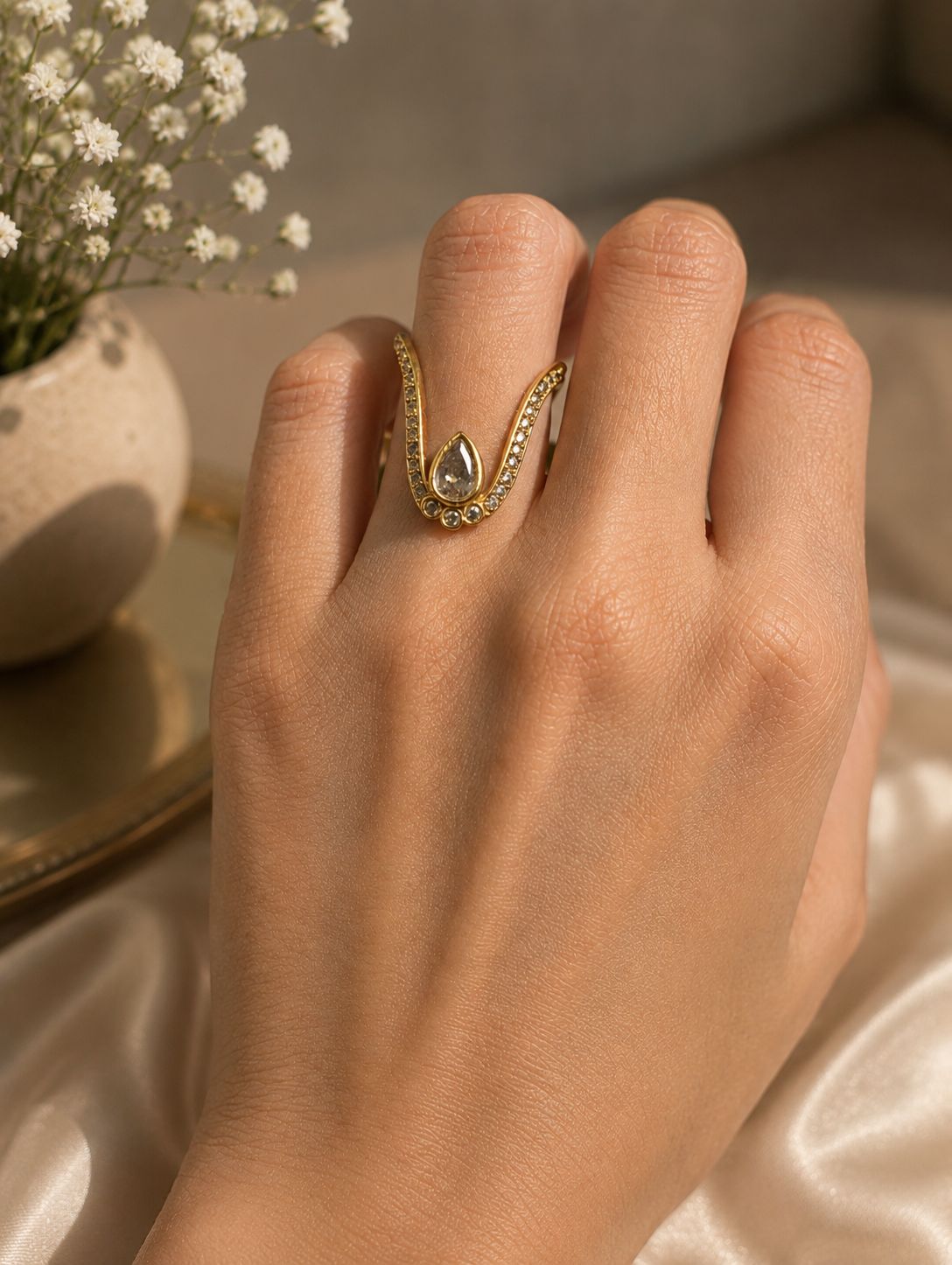 Close-up of a model wearing a gold-toned Vanki chevron ring on her index finger, featuring pave crystal accents along the V-curve and a central champagne white teardrop stone.