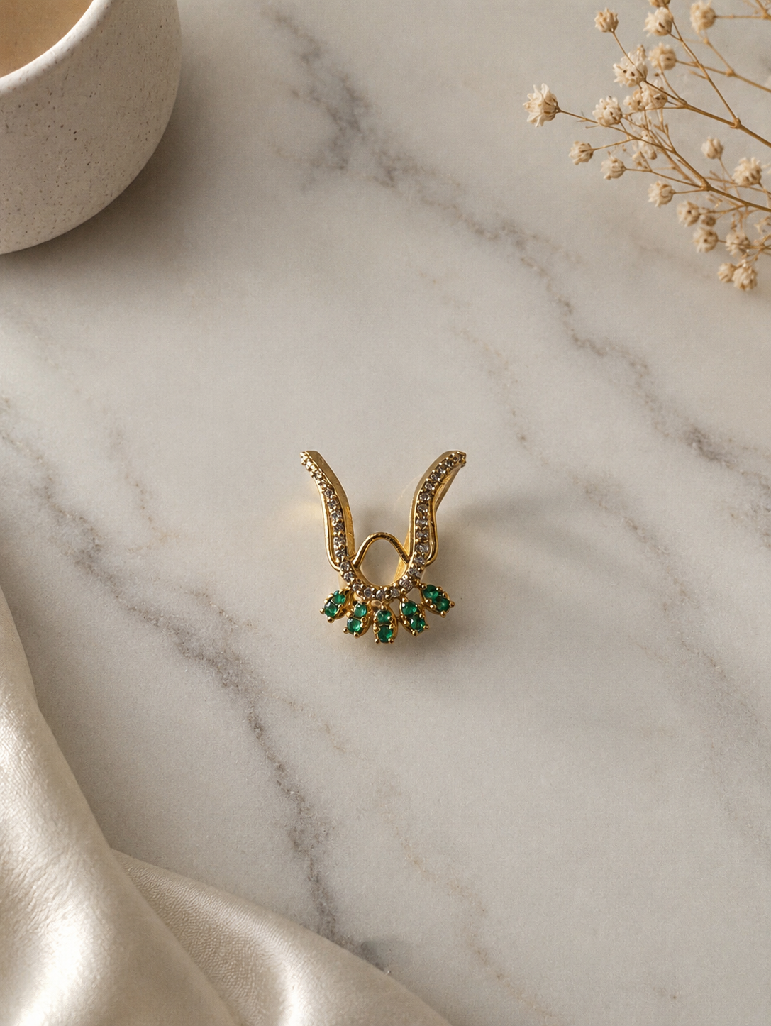 A gold-toned Vanki chevron ring featuring pave crystal detailing along the curved V-band and a fan-shaped border of five rich emerald-green stones.