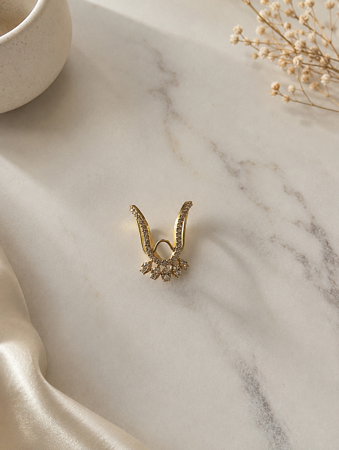 A gold-toned Vanki chevron ring featuring a pave clear crystal-paved V-shaped band and a lower fringe of five marquise-cut white cz stones resting on a marble background.