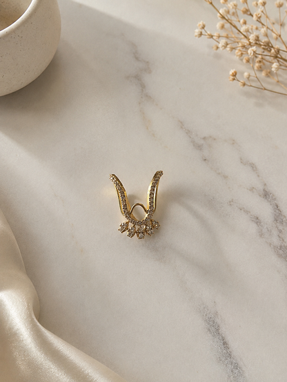 A gold-toned Vanki chevron ring featuring a pave clear crystal-paved V-shaped band and a lower fringe of five marquise-cut white cz stones resting on a marble background.