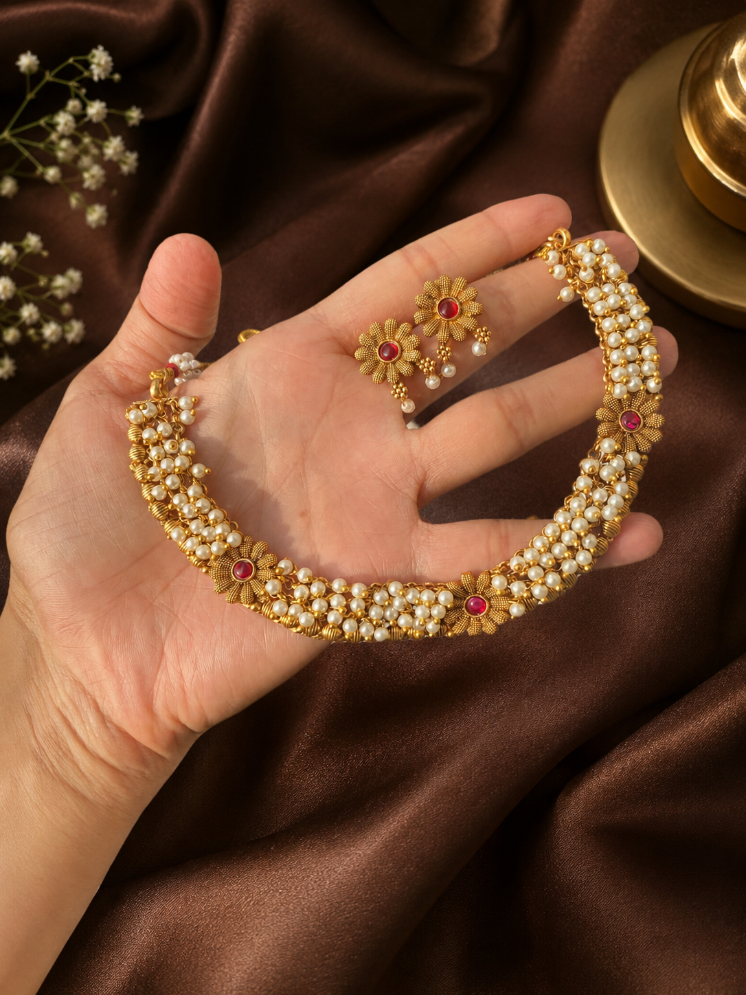 Gold and pearl jewelry set on a hand with a brown fabric background