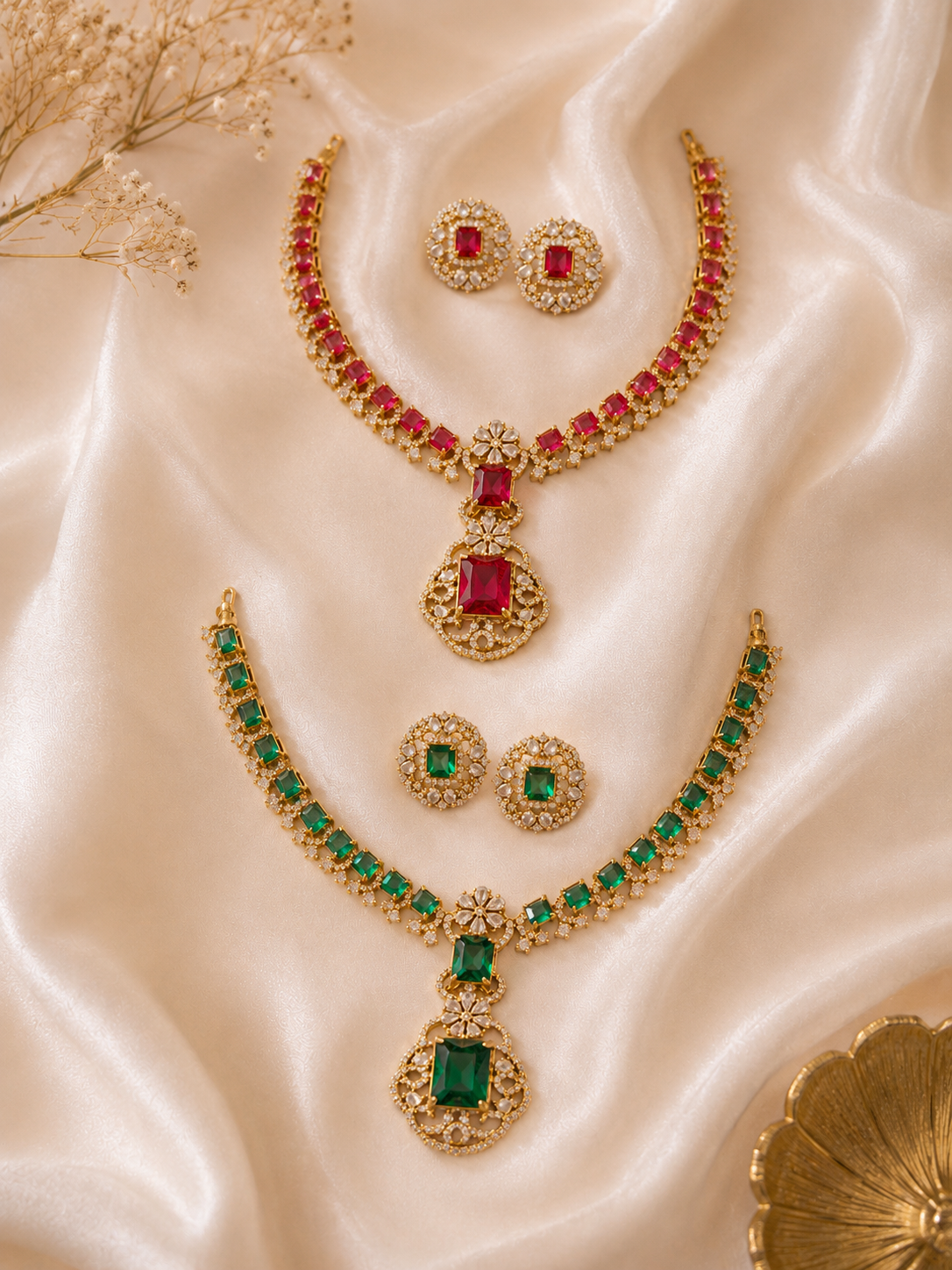 Two traditional gold-plated bridal choker necklace sets with matching round stud earrings, one featuring ruby red stones and the other emerald green stones, detailed with cubic zirconia diamonds on a white satin background.