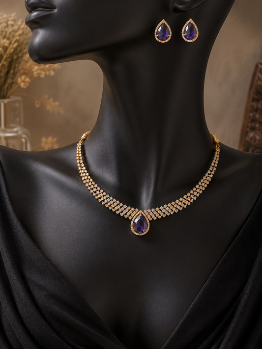An elegant gold-plated jewelry set displayed on a black mannequin, featuring a multi-row cubic zirconia choker necklace with a central teardrop-shaped purple amethyst stone and matching teardrop stud earrings.
