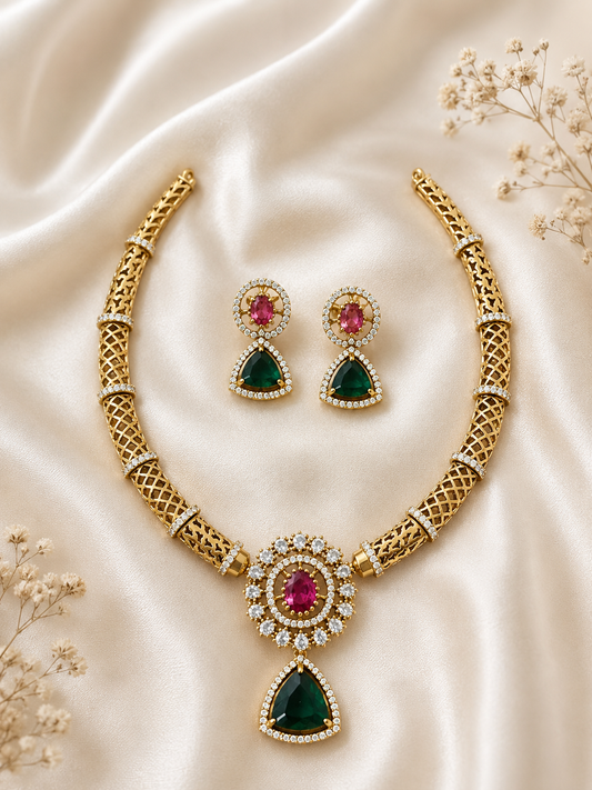 Premium gold-plated necklace set featuring a structured open-mesh lattice collar banded with sparkling CZ crystals. The central medallion boasts an oval pinkish-ruby stone ringed by crystals, ending in a dangling teardrop emerald charm. The matching geometric drop earrings rest in the center against a soft cream satin backdrop.
