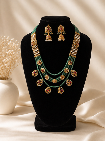 Green and gold necklace with matching earrings on a black stand against a beige background