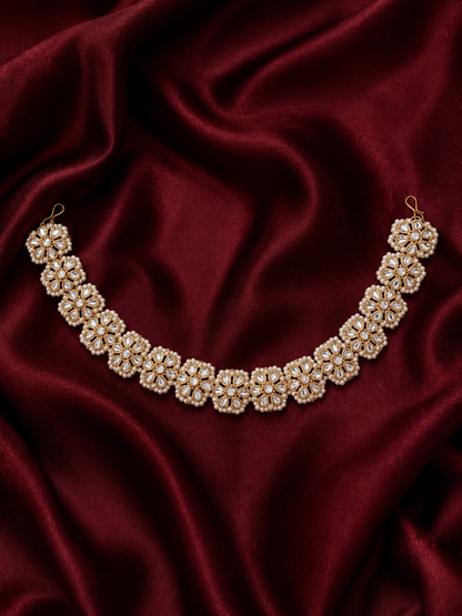 Traditional Indian gold-plated sheeshphool hair band featuring a continuous row of circular floral motifs set with glistening Kundan stones and tiny white pearls, shown laid flat on rich maroon satin fabric and modeled on a woman's hair.