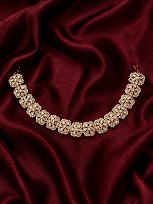 Traditional Indian gold-plated sheeshphool hair band featuring a continuous row of circular floral motifs set with glistening Kundan stones and tiny white pearls, shown laid flat on rich maroon satin fabric and modeled on a woman's hair.
