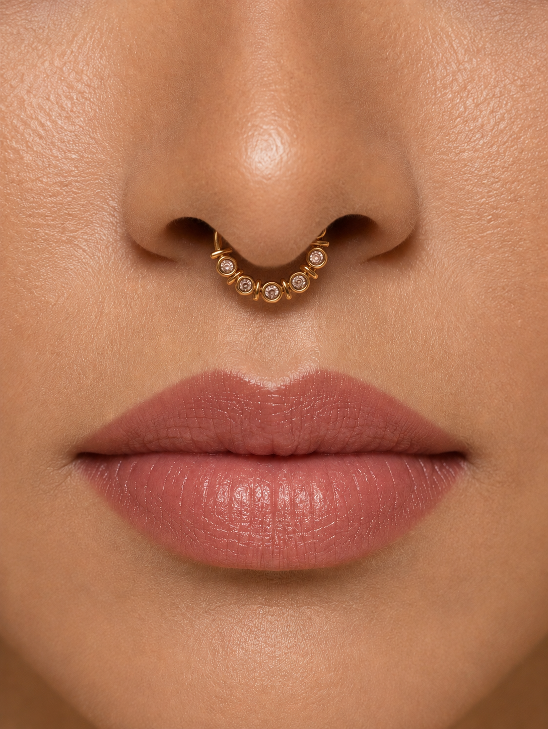 Close-up profile of a model wearing a gold-tone septum ring adorned with a row of five sparkling round bezel-set crystals.