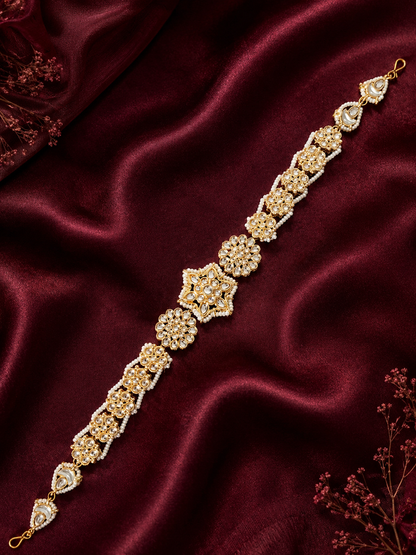 Heirloom-style gold-plated Indian sheeshphool headpiece featuring a central star-shaped Kundan medallion flanked by pearl-edged floral patterns, shown on a rich dark red satin backdrop and worn by a smiling model.