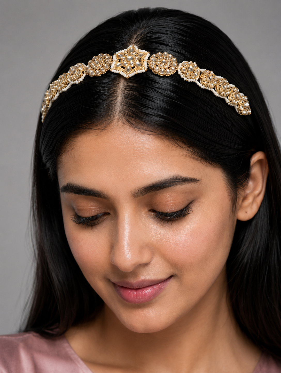 Heirloom-style gold-plated Indian sheeshphool headpiece featuring a central star-shaped Kundan medallion flanked by pearl-edged floral patterns, shown on a rich dark red satin backdrop and worn by a smiling model.