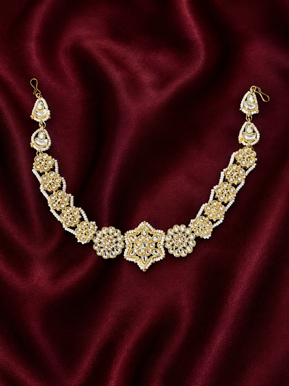 Heirloom-style gold-plated Indian sheeshphool headpiece featuring a central star-shaped Kundan medallion flanked by pearl-edged floral patterns, shown on a rich dark red satin backdrop and worn by a smiling model.