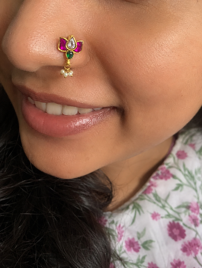 Close-up shot of a woman wearing a lotus-shaped Jadau Kundan non-piercing press-fit nose pin with ruby red and green stones and hanging pearl clusters.