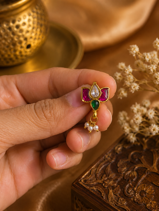 A person holding the SP013 traditional Indian Jadau Kundan lotus nose pin between their fingers, showcasing the intricate gold setting, vibrant pink, clear, and green gemstones.