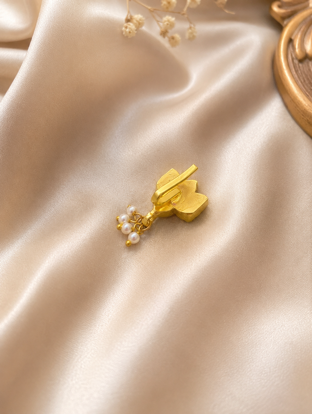 The reverse side mechanism of the SP013 gold-plated press-fit nose clip, displaying the non-piercing slide-on bar and hanging white seed pearls on a satin background.