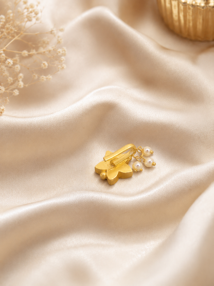 "Close-up detail of a handcrafted gold nose pin in a star design, featuring vibrant red stones and pearl drops, displayed on elegant beige fabric."