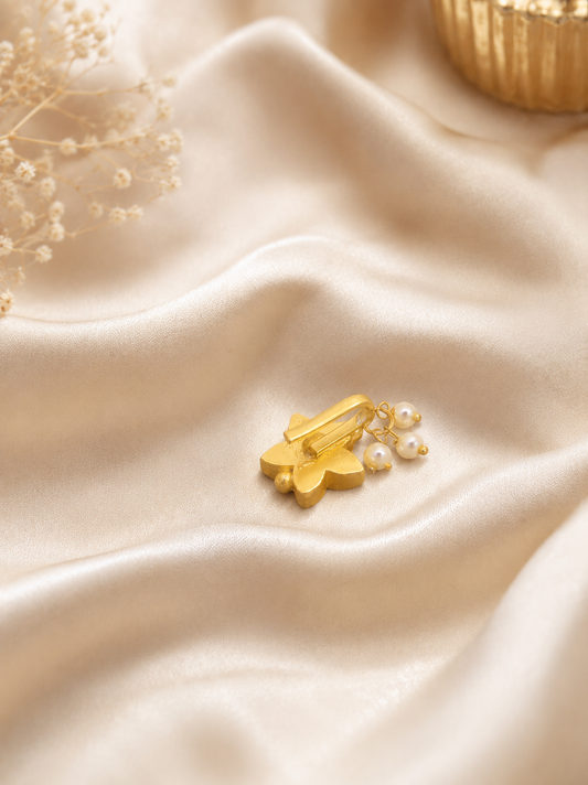 "Close-up detail of a handcrafted gold nose pin in a star design, featuring vibrant red stones and pearl drops, displayed on elegant beige fabric."