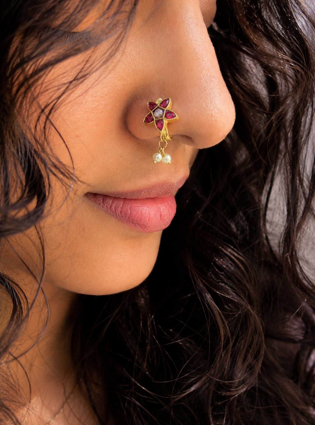 "A close-up portrait of a woman wearing an elegant, traditional gold star-shaped nose pin accented with red stones and pearls."