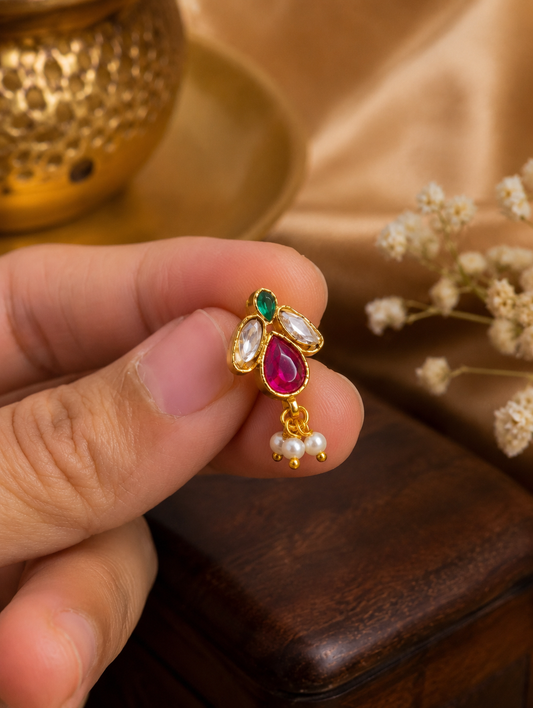 Close-up of a person holding the SP015 Jadau Kundan press-fit nose pin, showcasing the detailed pink teardrop stone, clear kundan accents, and dangling white pearls.