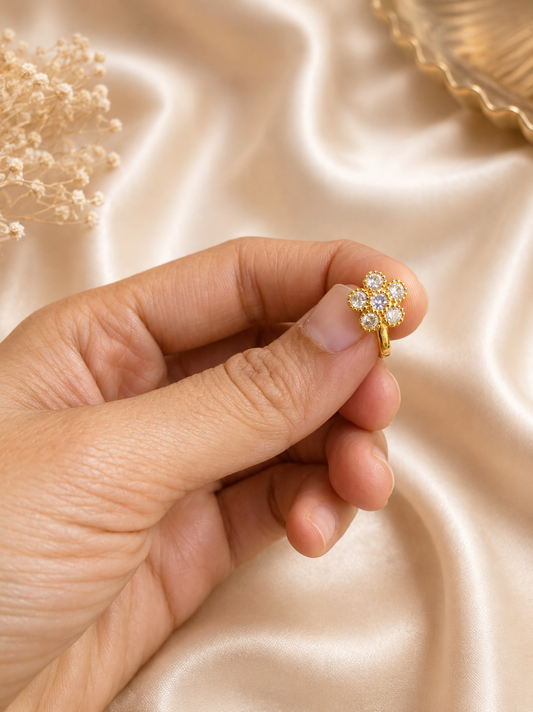 A hand holding the SP016 gold-toned floral press-fit nose pin, showing its front-facing design set with sparkling clear American Diamonds arranged like flower petals.
