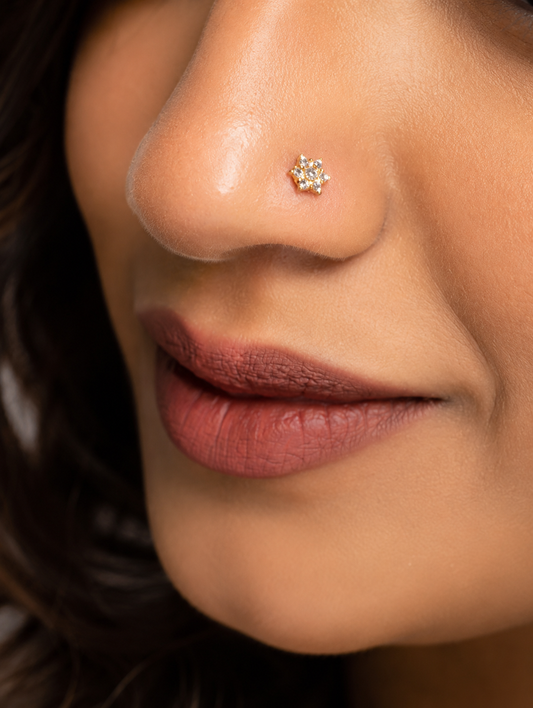 Close-up of a woman smiling subtly while wearing a delicate, star-shaped gold nose pin studded with seven sparkling diamonds arranged in a floral pattern.