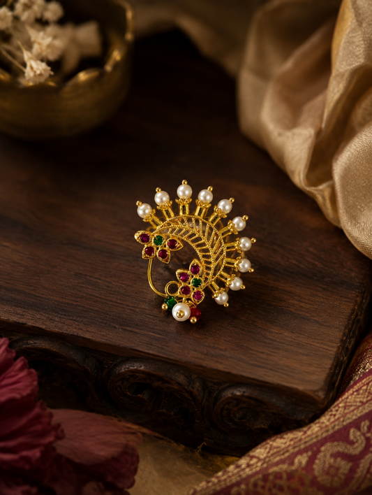 A gold-toned traditional Indian brooch featuring a Kairi motif adorned with white pearls and red, green, and white stones, displayed on a dark wooden surface. Maharashtrian Nath