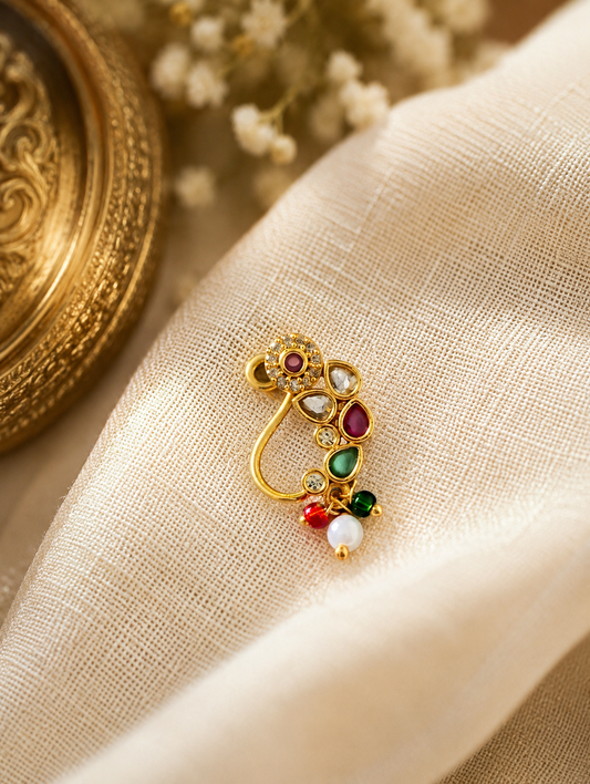 Woman wearing a gold-plated Maharashtrian nath styled with ruby-red, emerald-green, and clear stones with small hanging pearl drops.