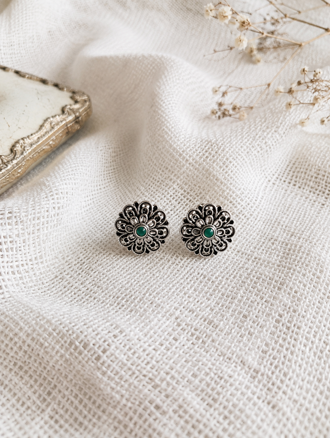 Floral earrings with green centers on a textured white fabric background