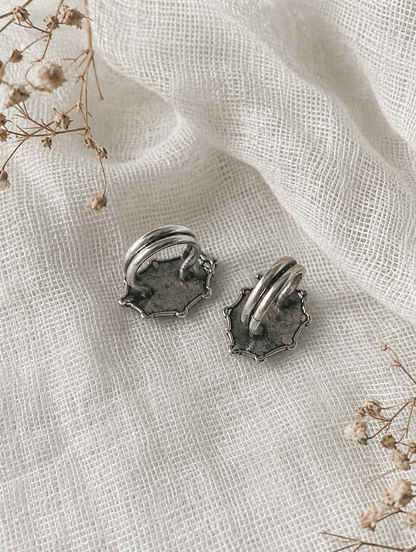 Pair of silver earrings on a textured white fabric background with dried flowers.