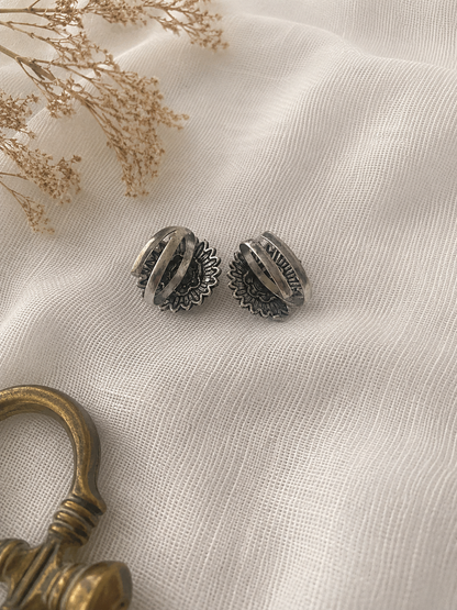 Pair of silver earrings on a textured beige fabric surface with dried flowers and a gold key.