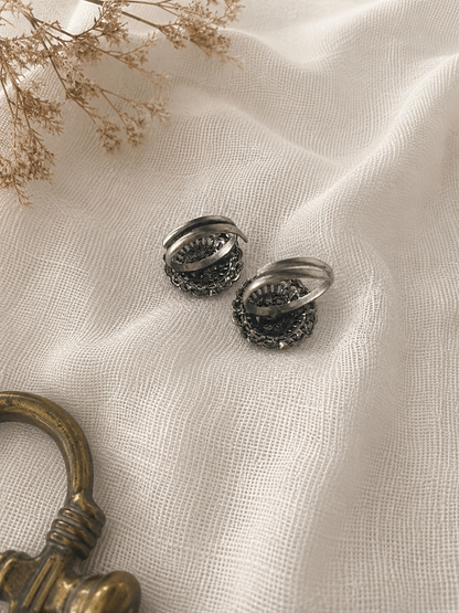 Pair of silver earrings on a textured white fabric surface with a small bouquet of dried flowers.
