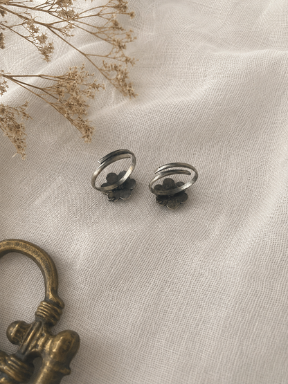Silver earrings on a textured beige fabric with dried flowers and a brass key.